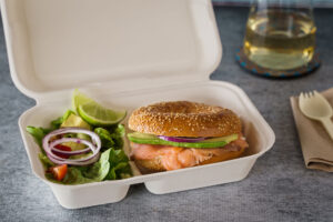 Salmon and avocado bagel with side salad in clamshell packaging