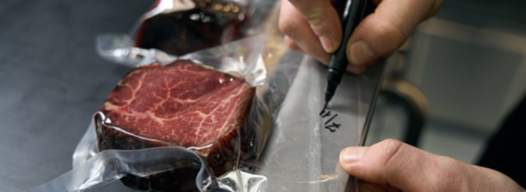 chef writing sealed date on piece of steak
